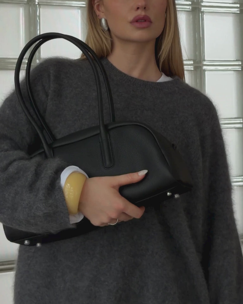 Woman styling the Lumi chunky butter yellow resin bangle with a grey oversized cashmere sweater and black leather handbag. A glossy statement resin bracelet designed for effortless everyday styling, capsule wardrobes, minimal fashion, Scandinavian-inspired outfits, and elevated neutral looks.