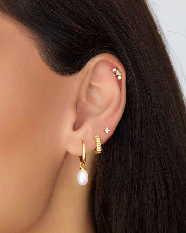 Curated ear stack featuring a gold flat back cartilage stud with a green pear-cut gemstone, paired with gold pearl drop earrings and minimalist studs for a layered look.