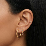 Close-up of a woman’s ear styled with a gold ear stack featuring a smooth gold hoop, a blue crystal huggie hoop, and a tiny star-shaped flat back stud in the upper cartilage. This image is for women looking for flat back earrings, cartilage piercings, and minimalist gold jewelry, showing how small, low-profile studs and hoops can be layered comfortably for everyday wear, sensitive ears, and a clean, modern ear stack.