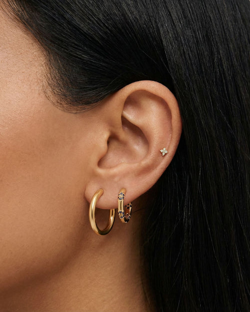 Close-up of a woman’s ear styled with a gold ear stack featuring a smooth gold hoop, a blue crystal huggie hoop, and a tiny star-shaped flat back stud in the upper cartilage. This image is for women looking for flat back earrings, cartilage piercings, and minimalist gold jewelry, showing how small, low-profile studs and hoops can be layered comfortably for everyday wear, sensitive ears, and a clean, modern ear stack.