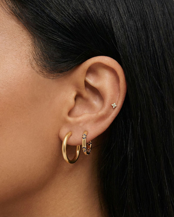 Close-up of a woman’s ear styled with a gold ear stack featuring a smooth gold hoop, a blue crystal huggie hoop, and a tiny star-shaped flat back stud in the upper cartilage. This image is for women looking for flat back earrings, cartilage piercings, and minimalist gold jewelry, showing how small, low-profile studs and hoops can be layered comfortably for everyday wear, sensitive ears, and a clean, modern ear stack.