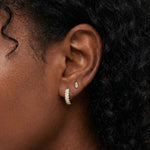 Close-up lifestyle image of a woman wearing Tia crystal gold hoop earrings on the lobe, styled with small gold stud earrings  and minimalist bar stud. Ideal for women looking for small gold crystal hoops that add refined sparkle, are lightweight for sensitive ears, and create an effortless, everyday ear stack with subtle shine.