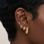 Close-up side profile of a blonde woman’s ear wearing a curated gold ear stack, featuring a twisted gold hoop earring, a slim pavé huggie, small marquise and round crystal studs, and a delicate cartilage stud. Designed for women with multiple piercings, this image helps customers visualise scale, placement, and layering of gold hoops and stud earrings to create a refined, cohesive everyday ear stack.