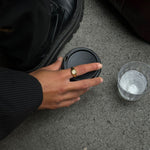 a hand holding a coffee wearing a textured gold filled ring with a white gemstone