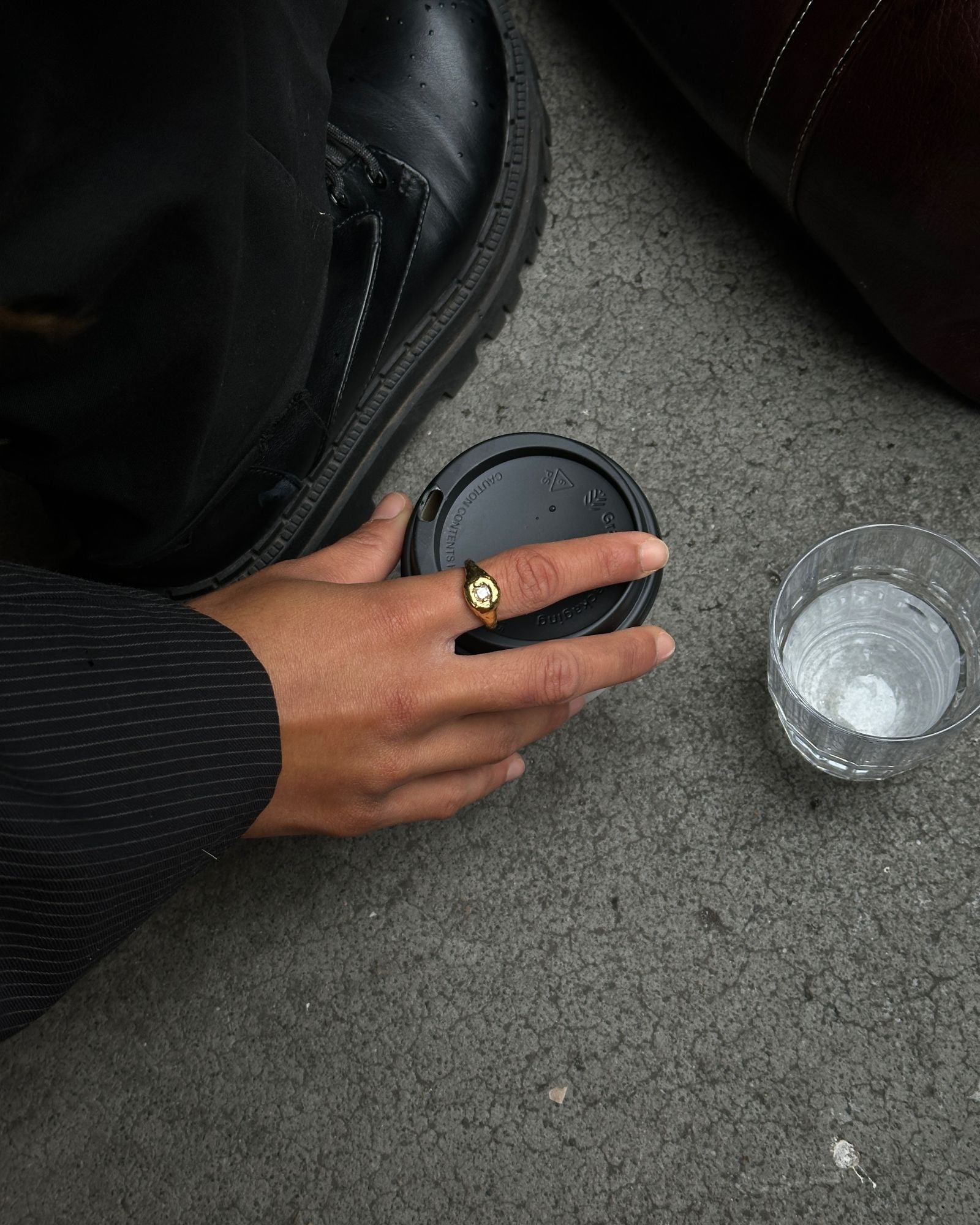 a hand holding a coffee wearing a textured gold filled ring with a white gemstone