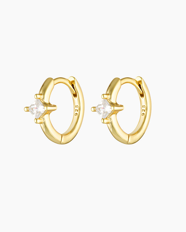 Pair of small gold huggie hoop earrings featuring a square-cut clear cubic zirconia set at the front, photographed on a clean white background. The image shows minimalist gold crystal huggie earrings crafted on a sterling silver base with gold plating, designed for women who want subtle sparkle without oversized hoops. Ideal for everyday wear, second piercings, or curated ear stacks, these earrings solve the need for lightweight, elegant hoop earrings that add polish while remaining comfortable, versatile, 