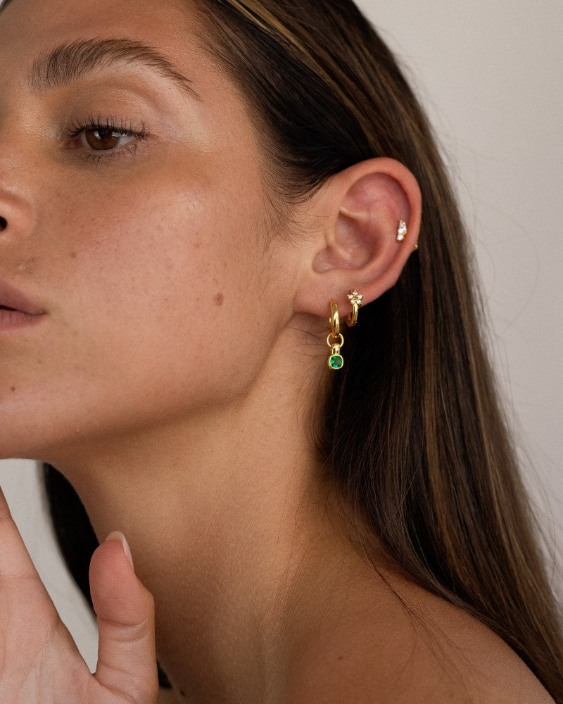 Alt text:

Close-up side profile of a woman wearing a layered gold ear stack featuring a flat back cartilage stud with small cubic zirconia stones, a gold huggie in the lobe, and a gold hoop with a green gemstone drop. The image shows how flat back earrings and cartilage studs can be styled for a modern, elegant ear stack, ideal for people seeking comfortable, secure jewellery for sensitive ears and everyday wear.