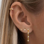 Close-up of an ear wearing gold flat back stud earrings including a crescent moon and star crystal design, paired with a slim gold cartilage hoop and a delicate crystal drop earring in the lobe. Shown on a model to demonstrate how flat back ear piercings sit flush against the ear, ideal for people building a curated ear stack who want secure, low-profile earrings that are comfortable for sensitive ears and suitable for all-day wear and sleeping.