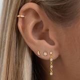 Close-up of an ear wearing gold flat back stud earrings including a crescent moon and star crystal design, paired with a slim gold cartilage hoop and a delicate crystal drop earring in the lobe. Shown on a model to demonstrate how flat back ear piercings sit flush against the ear, ideal for people building a curated ear stack who want secure, low-profile earrings that are comfortable for sensitive ears and suitable for all-day wear and sleeping.