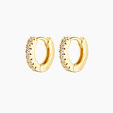 Pair of small gold huggie hoop earrings with a click-lock closure, set with clear cubic zirconia stones along the front, photographed on a white background. Designed for women seeking dainty gold hoop earrings, secure everyday huggies, and stackable earrings for second or third lobe, helix, or cartilage piercings, offering subtle sparkle without bulk or discomfort.