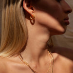 Close-up side profile of a woman wearing small polished gold hoop earrings and two layered gold chain necklaces resting along the collarbone. The image highlights minimalist gold jewellery styled on bare skin under warm natural light, emphasizing everyday elegance and layering versatility. Designed for women seeking timeless, understated jewellery that elevates daily outfits and solves the need for durable, easy-to-style pieces suitable for both casual and refined looks.