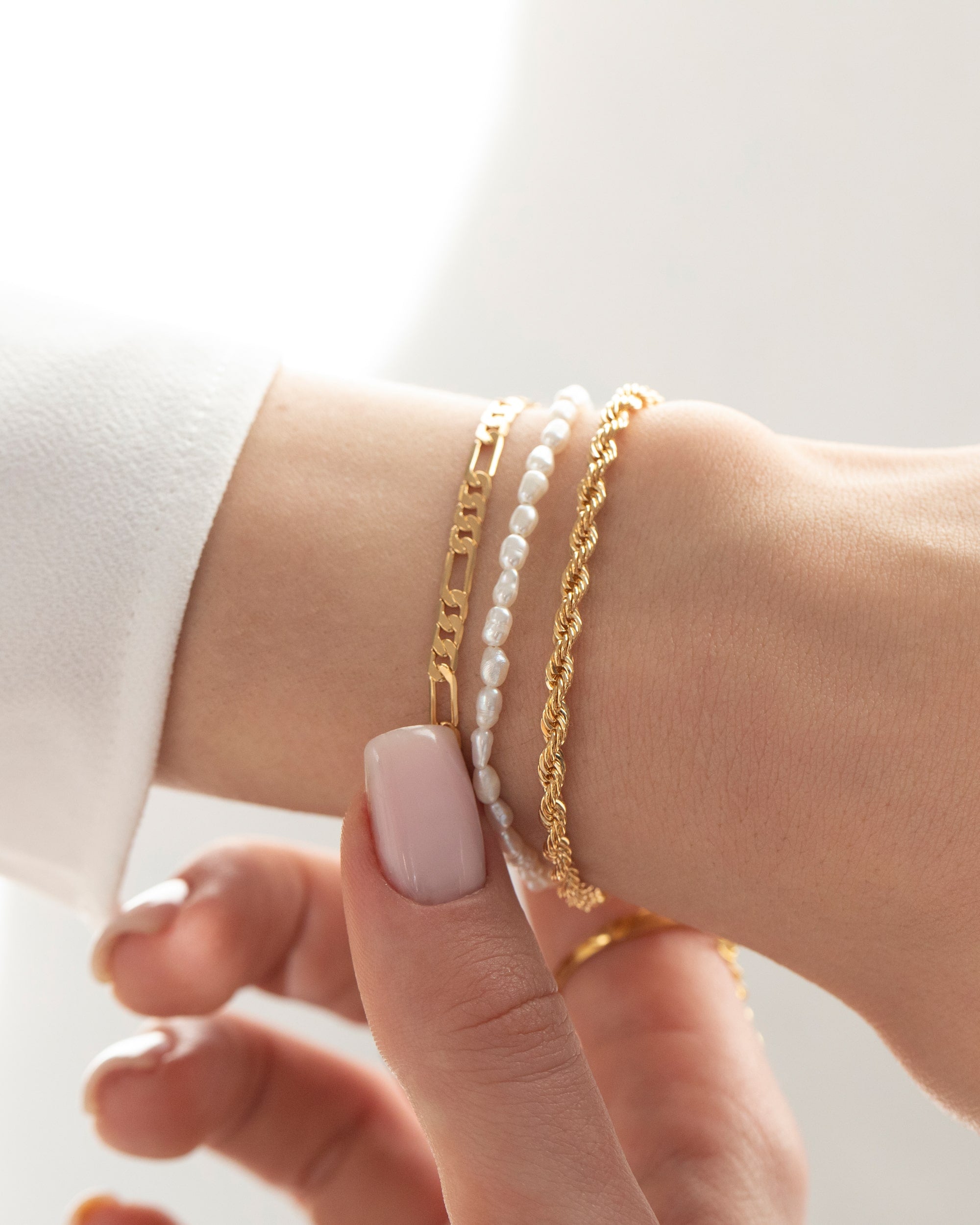 Close-up of a wrist wearing a freshwater pearl bracelet layered with gold chain bracelets, shown against a soft neutral background. Designed for women looking for a versatile everyday pearl bracelet that layers easily with gold jewellery and adds a refined, modern touch to casual and elevated outfits.