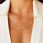 Layered gold necklaces worn on the neck, featuring a slim flat gold chain paired with a delicate gold rope chain, styled on skin with an open white shirt. This image is for women looking for everyday gold necklaces that layer cleanly without tangling and sit comfortably at the collarbone. It helps show necklace length, thickness contrast, and how minimalist gold chains create an elevated, effortless look suitable for daily wear and capsule wardrobes.
