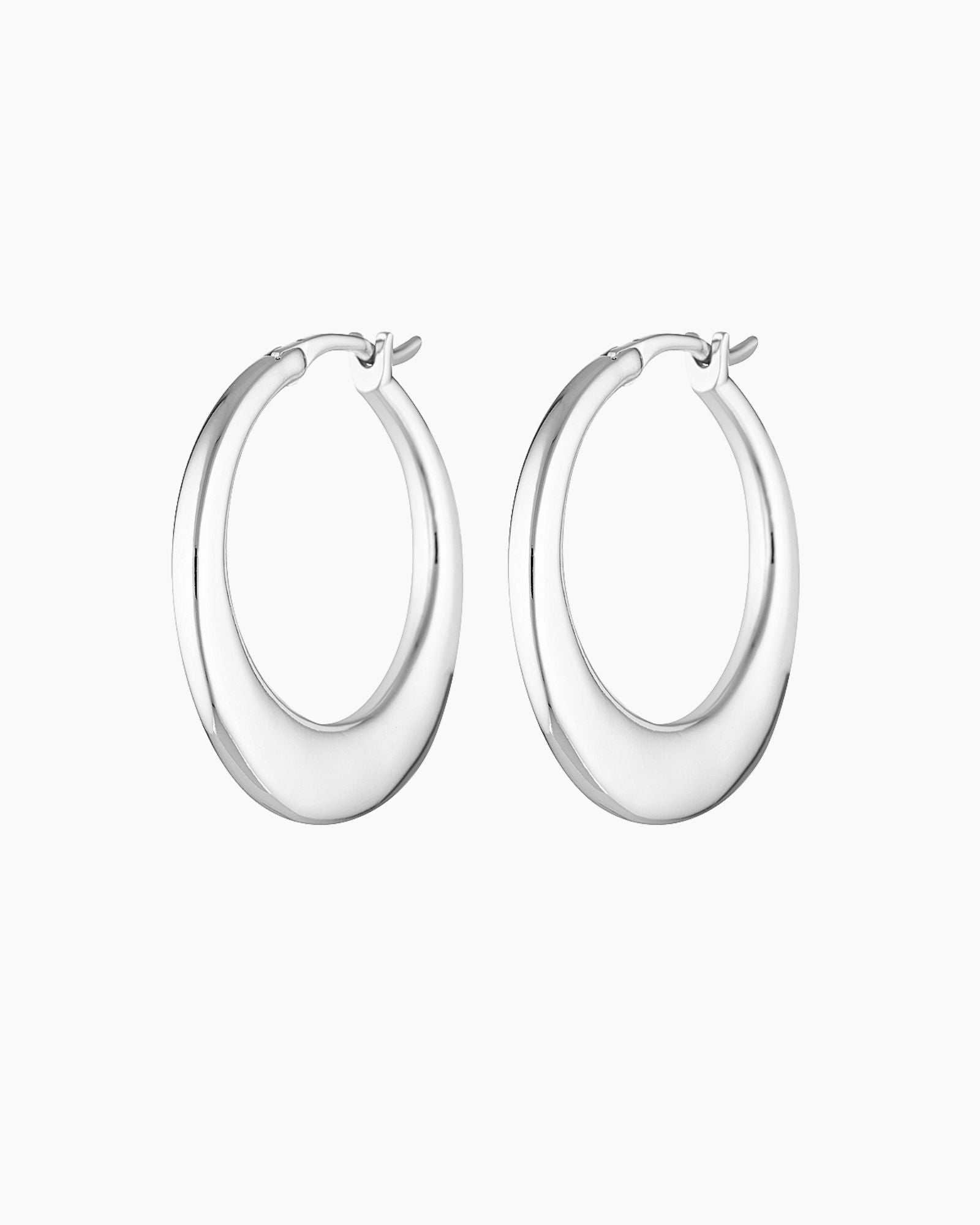 Product photo of a pair of medium-sized silver hoop earrings with a softly sculpted, rounded silhouette and high-polish finish, displayed on a clean white background. The hoops feature a smooth hinged closure and a refined, minimalist shape that reflects light evenly, highlighting their modern design. Designed for women seeking elegant silver hoop earrings that feel elevated yet wearable, this image showcases statement hoops suitable for everyday wear, special occasions, and sensitive ears. Ideal for custom