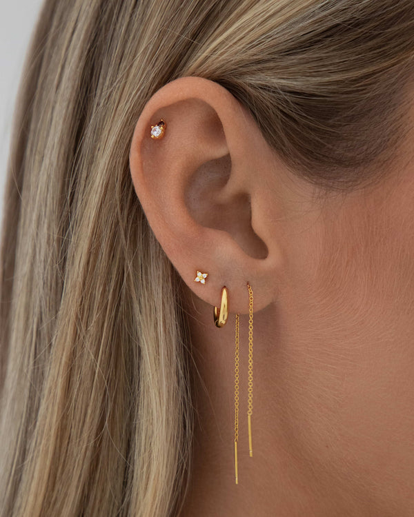 Close-up of a woman’s ear styled with a minimalist gold ear stack, featuring a dainty flower stud earring in the lobe, a small gold hoop, a delicate gold chain drop earring, and a tiny crystal flat-back stud in the upper cartilage. Designed for women seeking refined, everyday earrings for lobe and cartilage piercings, this image highlights comfortable, lightweight jewellery ideal for sensitive ears and effortless ear stacking.